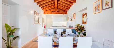 Uma zona de refeições moderna com teto de madeira, paredes brancas e cozinha ao fundo.