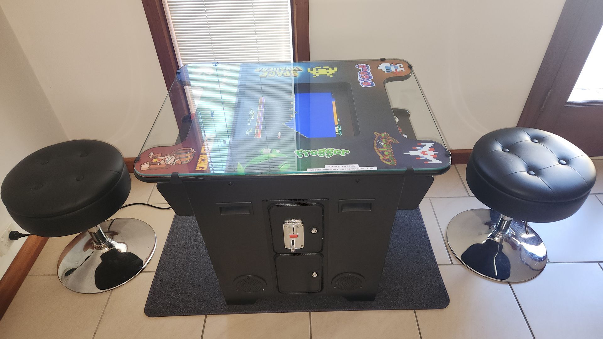 A retro arcade machine with a glass top, two stools, and a control panel.