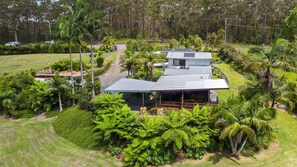 Ein modernes, zweistöckiges Haus mit einer großen Terrasse, umgeben von üppiger Vegetation und einem gepflegten Rasen.