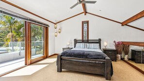 Ein Schlafzimmer mit einem großen Bett, einem Deckenventilator, einem Nachttisch, einer Lampe und Blick ins Freie durch eine Schiebetür.