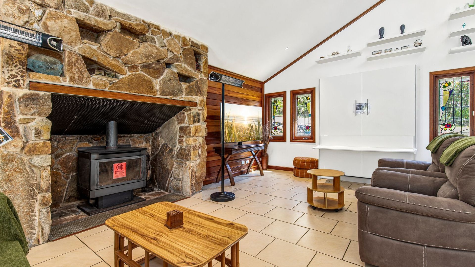 A cozy living room with a stone fireplace, wooden furniture, and a white cabinet.