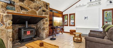 A cozy living room with a stone fireplace, wooden furniture, and a white cabinet.