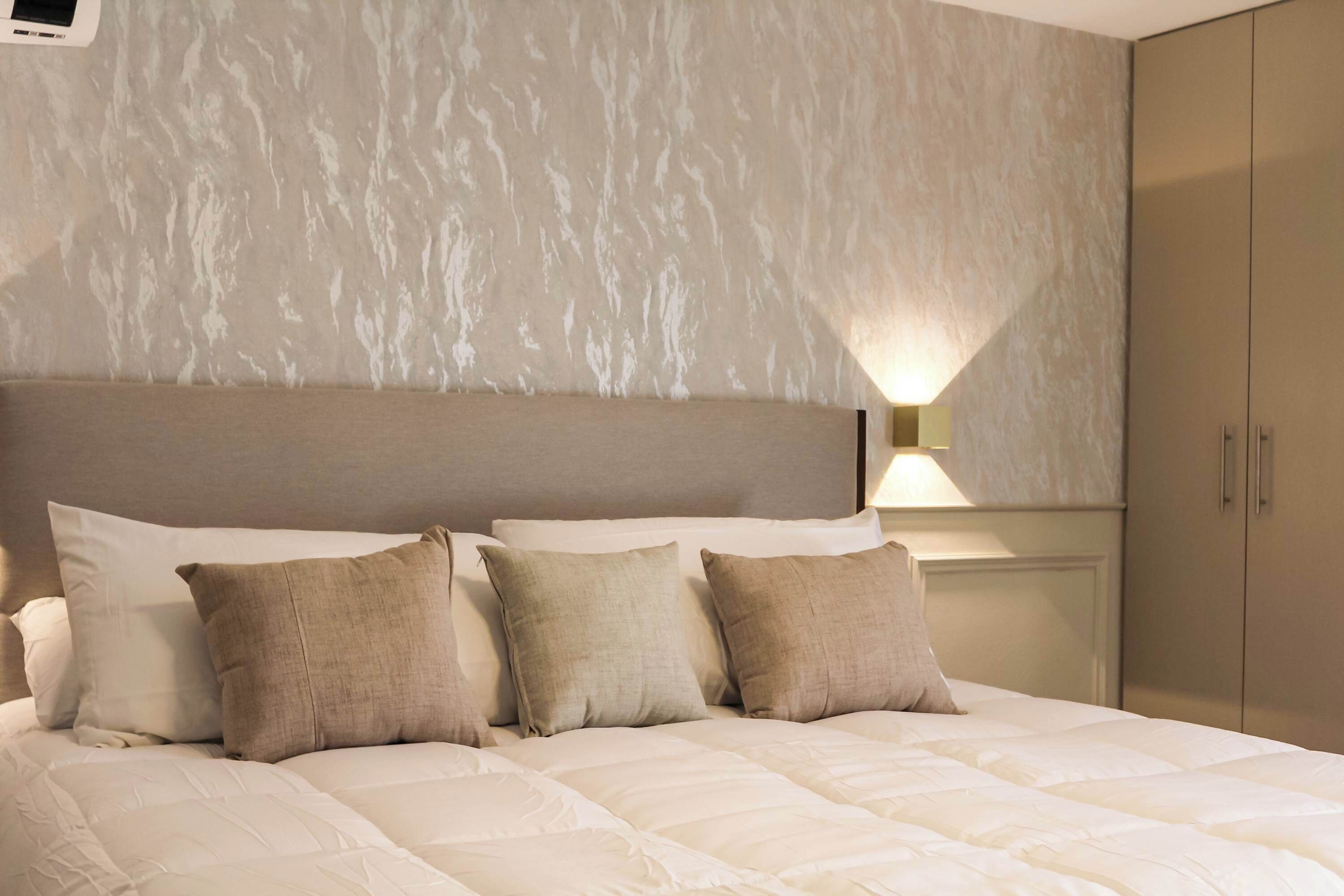 Ein Hotelzimmer mit Bett, Kissen, Kopfteil, einer Wandlampe und einem Kleiderschrank.
