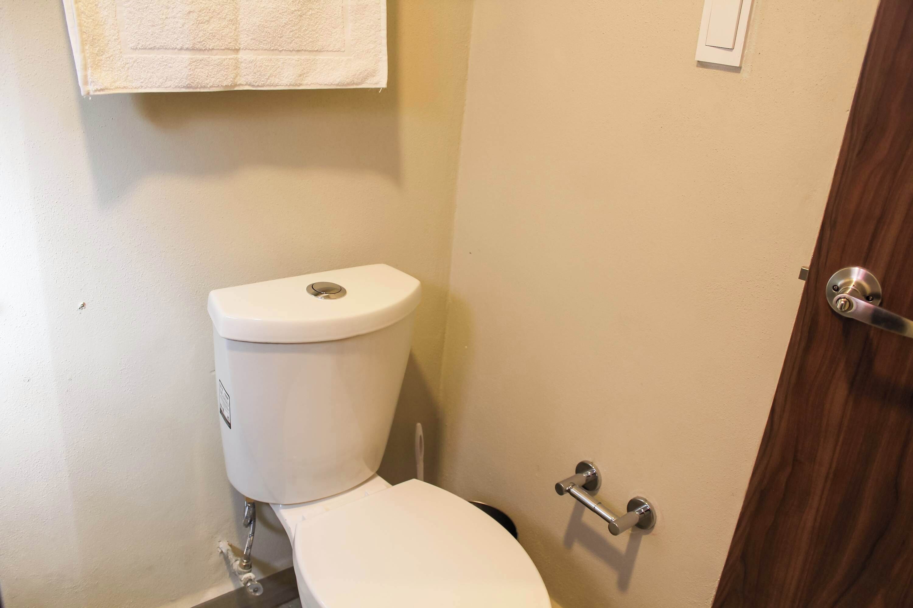 Une petite salle de bain avec des toilettes, une serviette accrochée au mur et une porte dotée d’une poignée.