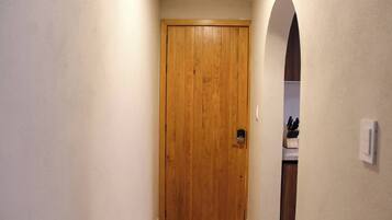 A wooden door in a hallway with a light switch on the wall and a knife block in the background.