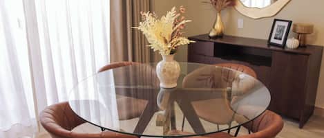 A modern room with a glass table, two brown leather chairs, a vase with dried flowers, a mirror, and a dark wooden cabinet.
