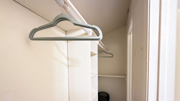 Um corredor com uma porta branca, um cesto de lixo preto e um cabideiro com um porta-roupas.