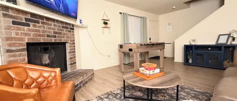 A living room with a leather sofa, a fireplace, a foosball table, and a television displaying a show.