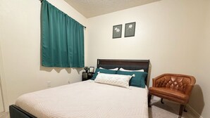 Quarto com cama, mesa de cabeceira, luminária, cadeira e duas quadros pendurados na parede.