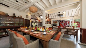 A spacious dining area with a wooden table set for breakfast, surrounded by wicker chairs with orange cushions. - Villa Hangat by Villa Finder (Badung)
