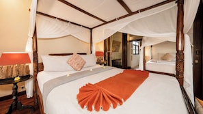 Ein Himmelsbett mit weißer Bettdecke und einer dekorativen orangefarbenen Tagesdecke.