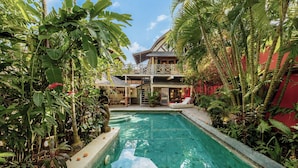 Une piscine entourée de plantes tropicales, avec une maison en arrière-plan.