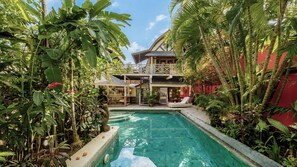Ein Poolbereich mit einem Haus im Hintergrund, umgeben von tropischen Pflanzen.