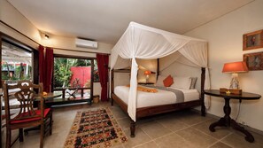 A bedroom with a four-poster bed, a wooden chair, a small table, and a view of the outdoors. - Villa Hangat by Villa Finder (Badung)