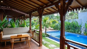 Un espacio al aire libre cubierto con piscina, mobiliario de madera y abundante vegetación.