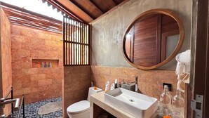 Un baño moderno con pared de piedra, puerta de madera, lavamanos blanco y espejo redondo.