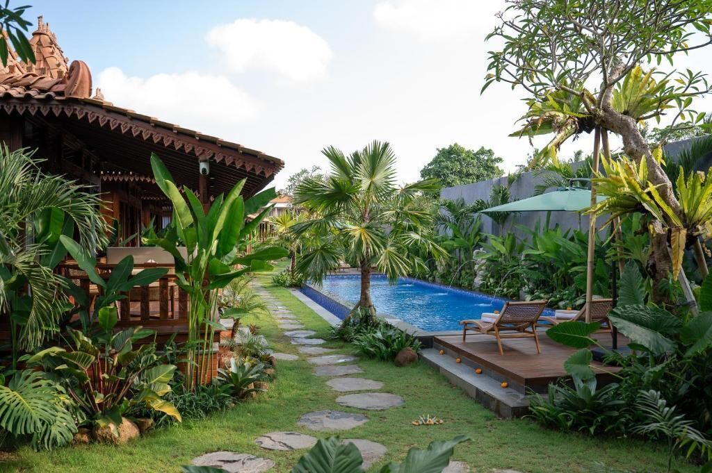 Un área de piscina con terraza de madera, sillas de descanso y plantas tropicales.