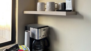 Een keukenhoek met een koffiezetapparaat, mokken, een WiFi-bordje en een mand vol koffievoorraad.
