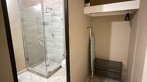 Een badkamer met een douchecabine van glas, een witte wastafel en een handdoekrek.