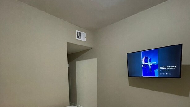Een slaapkamer met een bed, een aan de muur bevestigde televisie en een deur naar een andere kamer.
