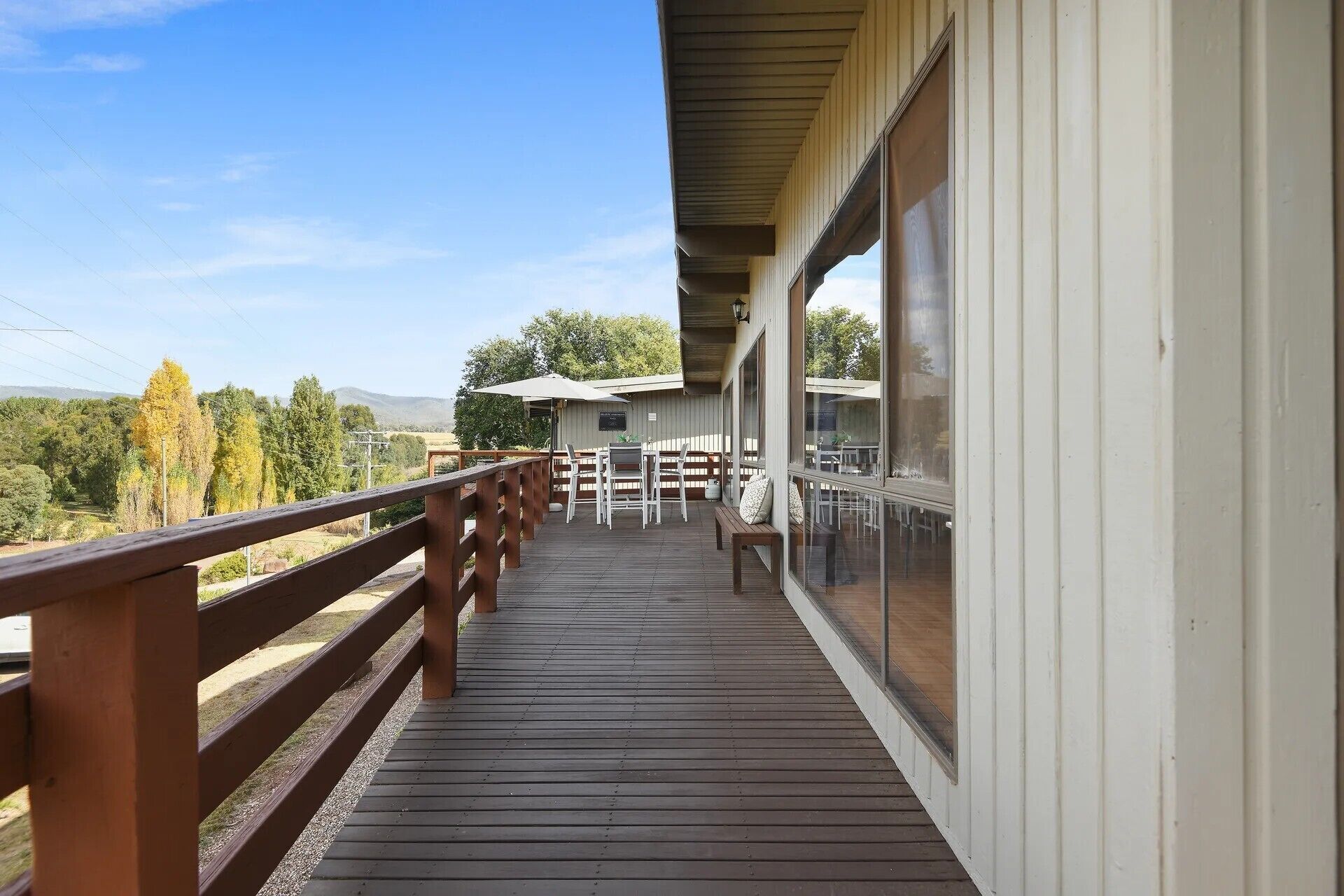 Una terraza de madera con barandilla, un espacio de descanso cubierto y vistas del paisaje circundante.