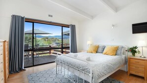 A bedroom with a bed, bedside table, lamp, and a view of the outdoors. - Red Gum - enjoy superb views in the heart of Merrijig! Sleeps 9 (Merrijig)