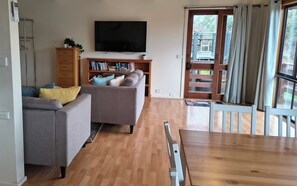 A living room with a sofa, a television, a bookshelf, and a dining area with a table and chairs. - Red Gum - enjoy superb views in the heart of Merrijig! Sleeps 9 (Merrijig)