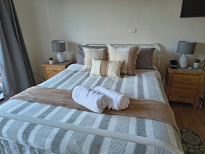 A neatly made bed with striped bedding and a folded towel, two bedside tables with lamps, and a power outlet on the wall. - Red Gum - enjoy superb views in the heart of Merrijig! Sleeps 9 (Merrijig)
