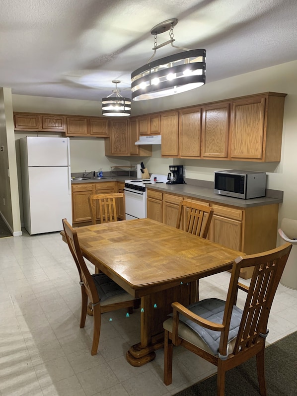 A kitchen with wooden cabinets, a refrigerator, stove, microwave, and a dining table with chairs.