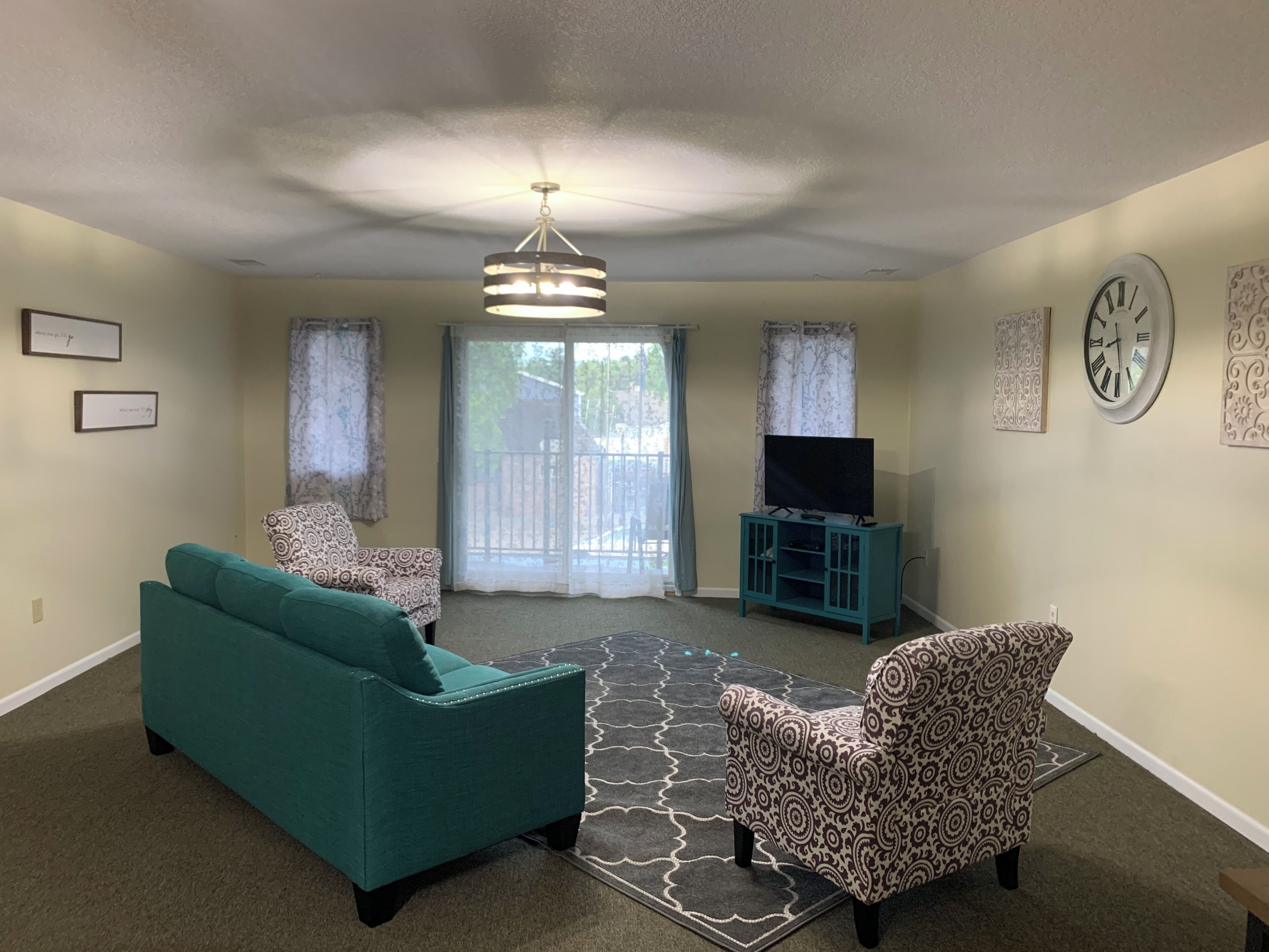 A living room with a teal sofa, patterned armchair, and a television on a stand.