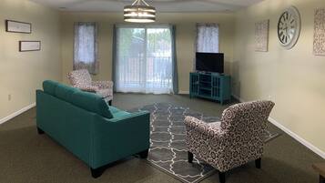 A living room with a teal sofa, patterned armchair, and a television on a stand.