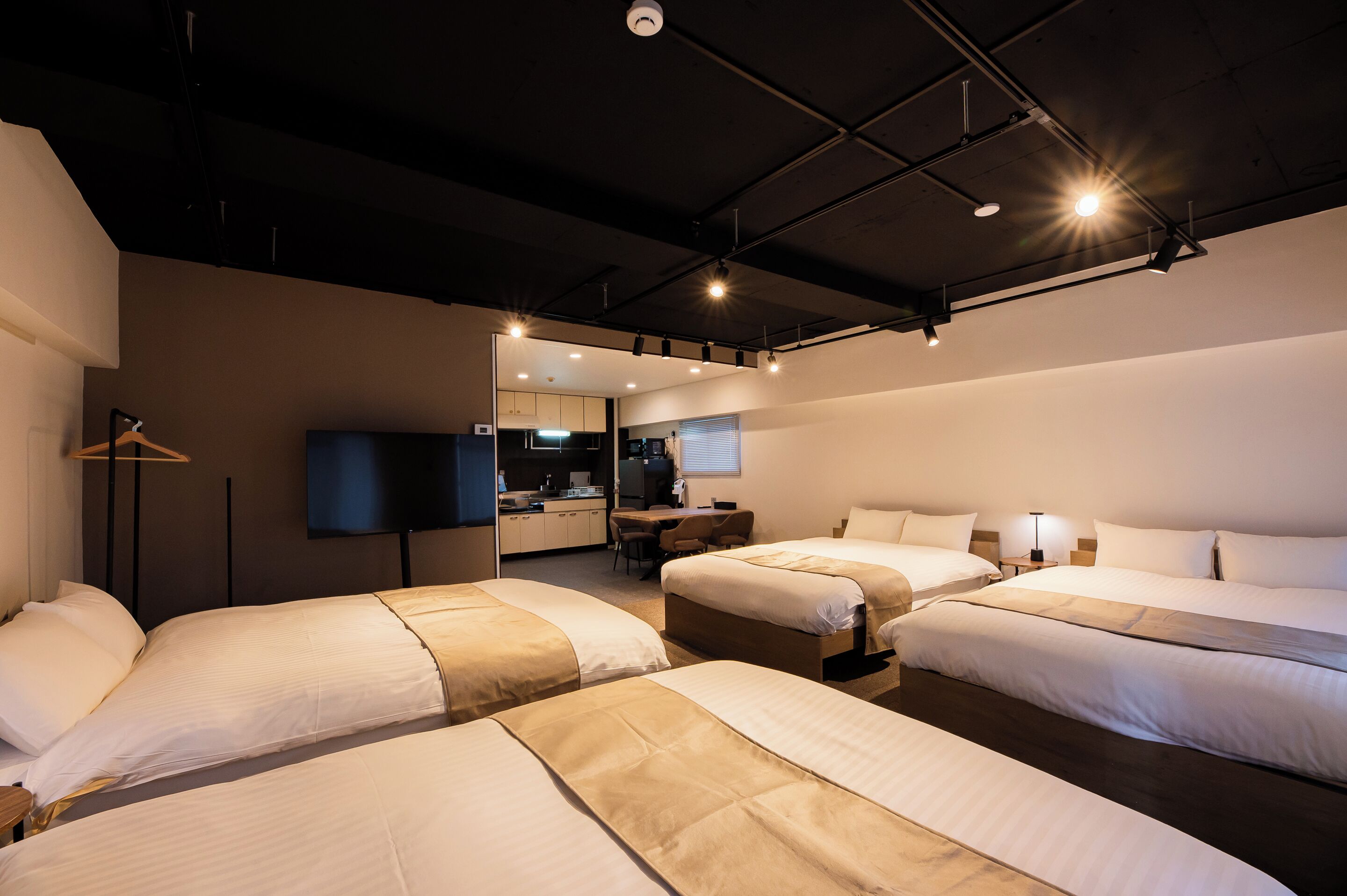 A hotel room with two beds, a desk, a television, and a kitchenette.