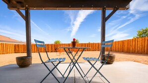Eine Terrasse im Freien mit Tisch und Stühlen, einem Holenzaun und blauem Himmel.