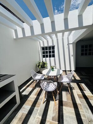 Eine Terrasse mit einem runden Tisch, vier Stühlen, einem Blumentopf und einem Fenster.