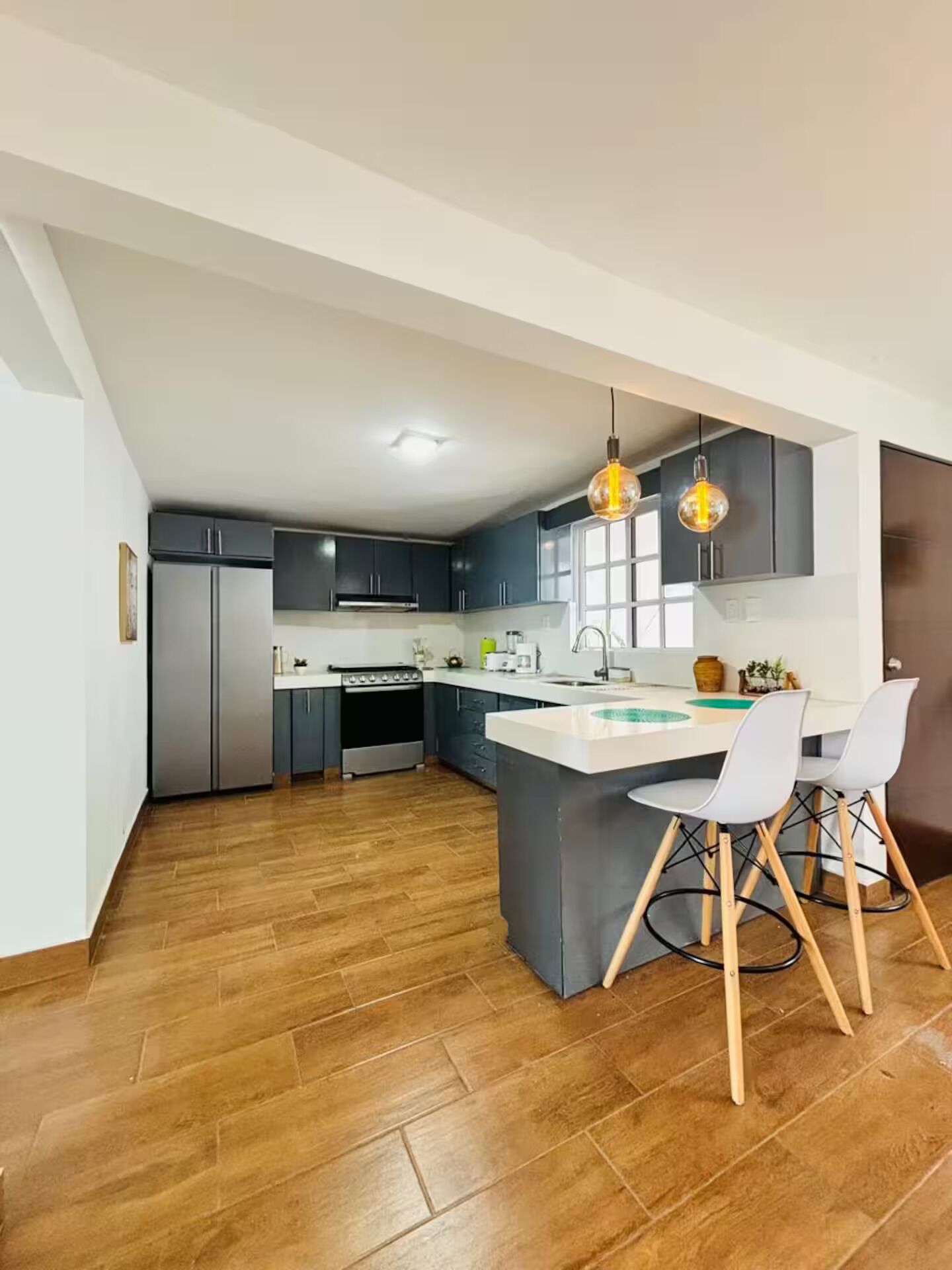 A modern kitchen with a central island, dark cabinets, and a wooden floor.