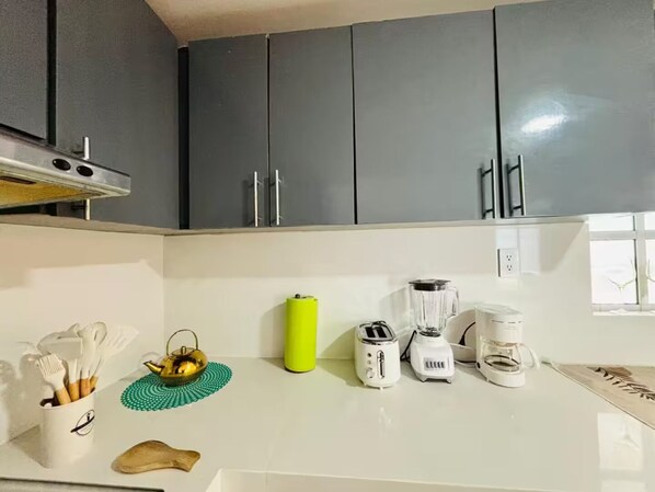 Eine Küche mit grauen Schränken, einer weißen Arbeitsplatte und verschiedenen Geräten, darunter ein Toaster, ein Mixer und eine Kaffeemaschine.