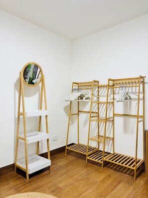 Una habitación con piso de madera, pared blanca y una estantería de madera con ropa colgada.