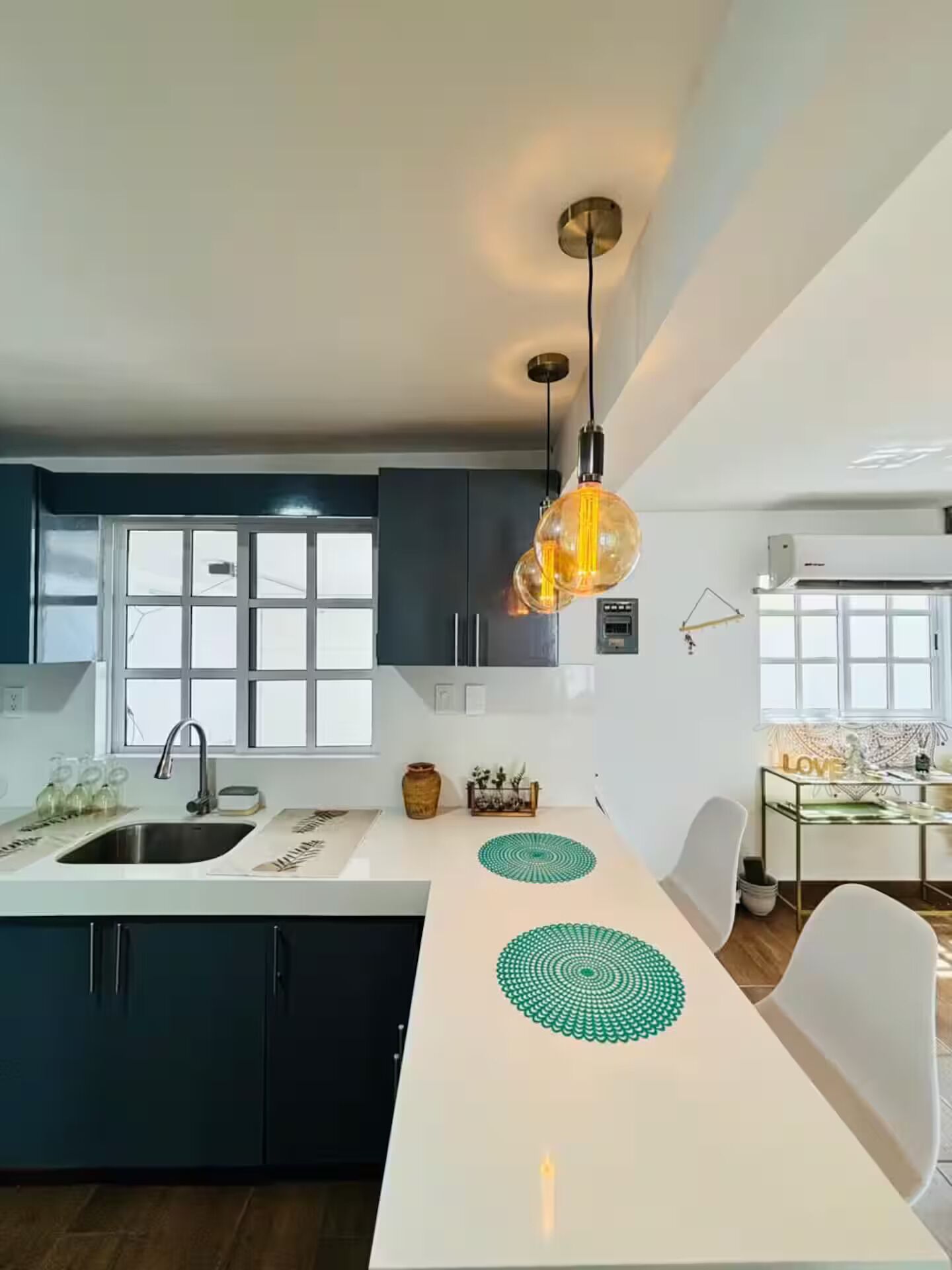 A modern kitchen with a central island, pendant lighting, and a view of the dining area.