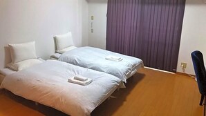 Una habitación con dos camas, una silla y un ventanal con cortinas.