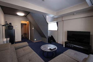 A modern living room with a flat-screen TV, a sofa, a coffee table, and a staircase. - The Lang Hotel Fukuoka (Fukuoka)