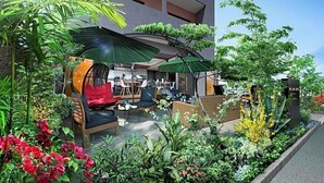 Un área de estar al aire libre con mesas y sillas, rodeada de abundante vegetación y plantas.