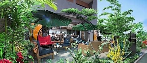 An outdoor seating area with tables and chairs, surrounded by lush greenery and plants.