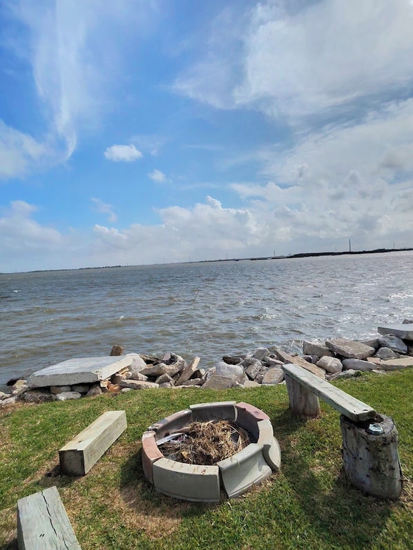 A lakeside view with a fire pit, wooden benches, and a grassy area.