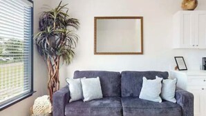 Ein Zimmer mit grauem Sofa, einem großen Spiegel, einem Topfpflanzen und einem weißen Schrank.