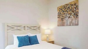 Ein Bett mit weißem Kopfteil, blauen Kissen und einer blauen Tagesdecke.