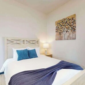 Un lit avec une tête de lit blanche, des oreillers bleus et un plaid bleu.