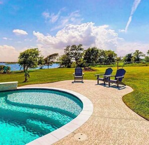 A swimming pool with two Adirondack chairs and a grassy area with trees.