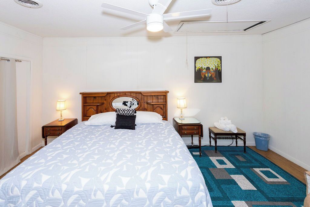 Habitación de hotel con una cama grande, dos mesitas de noche, un ventilador de techo, un cuadro en la pared y una alfombra azul estampada.