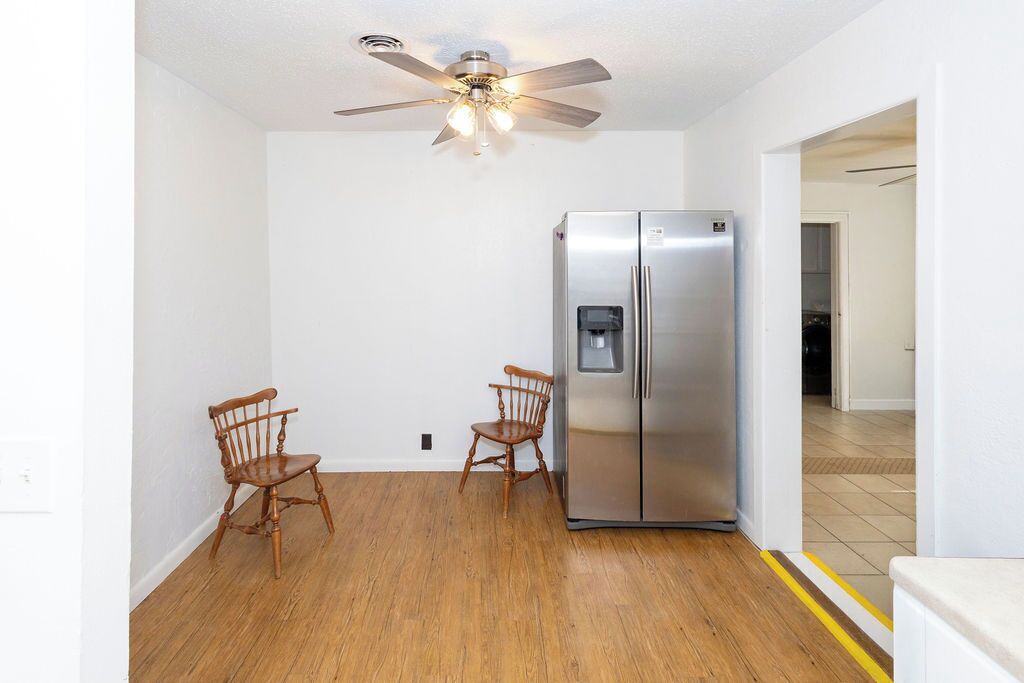 Une cuisine équipée d’un réfrigérateur en acier inoxydable, de chaises en bois et d’un ventilateur de plafond.