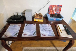 A table with a remote control, a book, a box labeled '300', and three informational cards titled 'Clean up', 'House Rules', and 'Welcome to Zara's Cottage'.